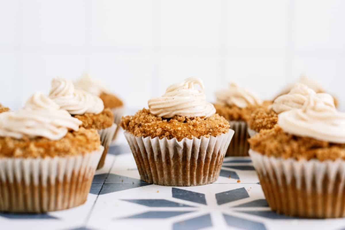 A group of cupcakes with beige frosting on a patterned surface.