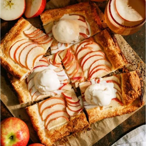 An apple tart cut into 6 squares some topped with a scoop of ice cream. Fresh apples on the side.