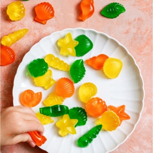 A plate of Homemade Jello Fruit Snacks with a little hand grabbing one.
