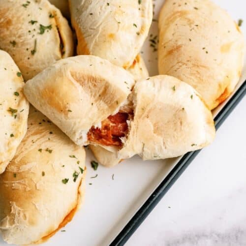 Baked Pizza Pockets on a white serving tray with on split in half to see the inside.