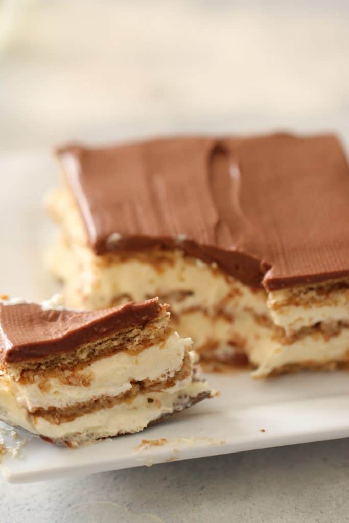 A slice of No Bake Eclair Cake on a plate with the remaining cake in the background.