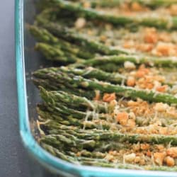 Glass dish containing roasted asparagus spears topped with breadcrumbs and grated cheese.