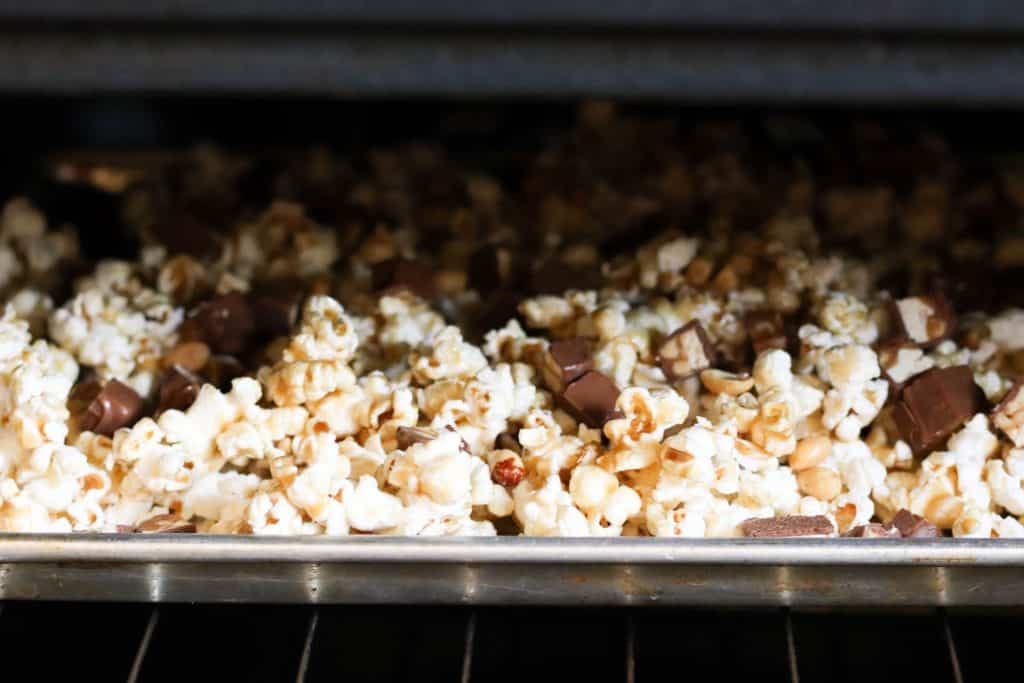 Snickers Popcorn in the oven on a sheet pan.